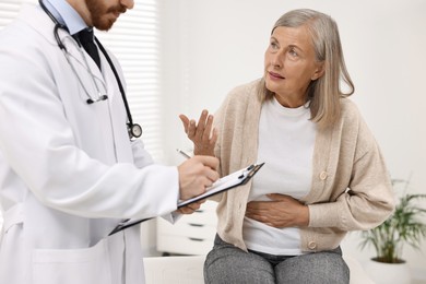 Doctor consulting senior patient with stomach pain in clinic, closeup