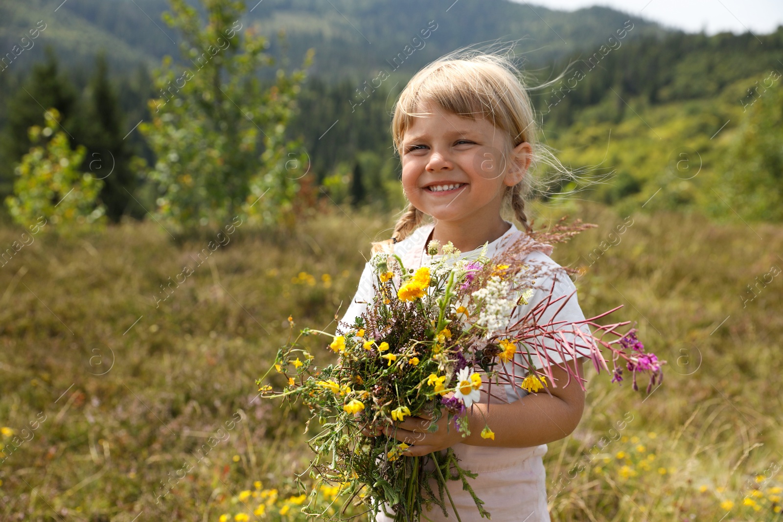 Photo of Smiling little girl with bouquet of wildflowers at field. Child enjoying beautiful nature