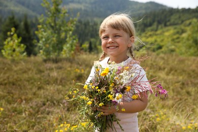 Smiling little girl with bouquet of wildflowers at field. Child enjoying beautiful nature