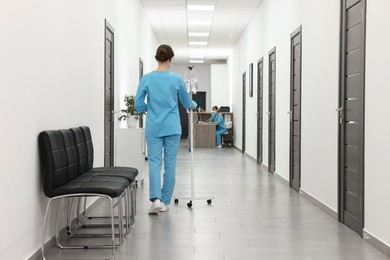 Photo of Nurse with IV drip in hospital hallway, back view