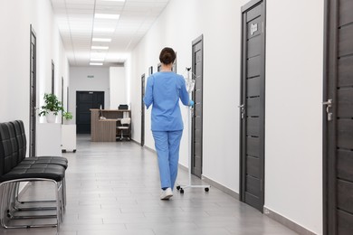 Nurse with IV drip in hospital hallway, back view