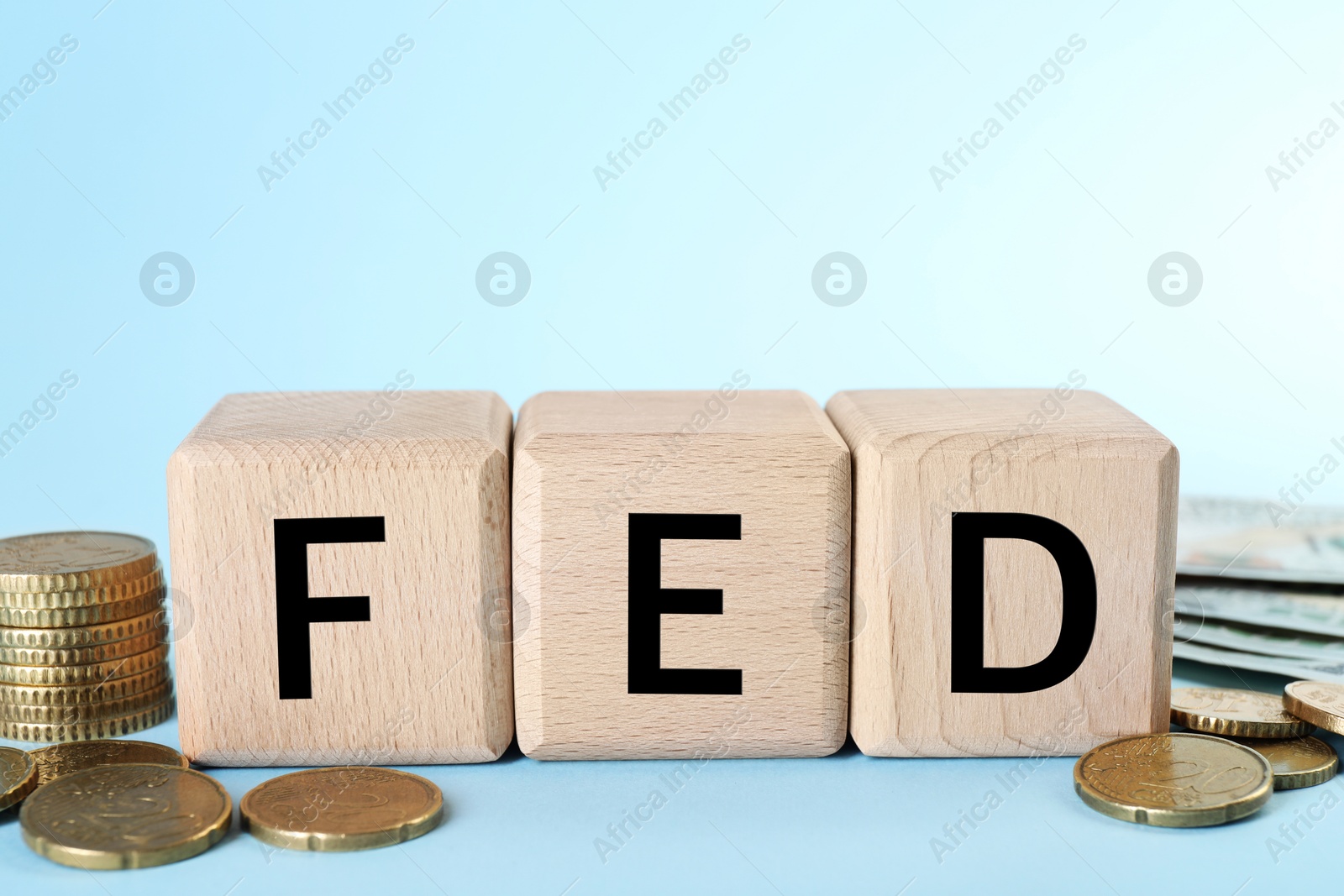 Photo of Wooden cubes with letters Fed (Federal Reserve System) and coins on light blue background, closeup