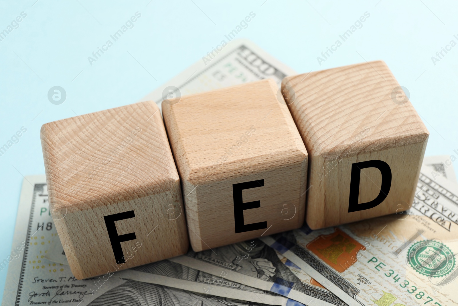 Photo of Wooden cubes with letters Fed (Federal Reserve System) and dollar banknotes on light blue background, closeup