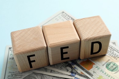 Photo of Wooden cubes with letters Fed (Federal Reserve System) and dollar banknotes on light blue background, closeup