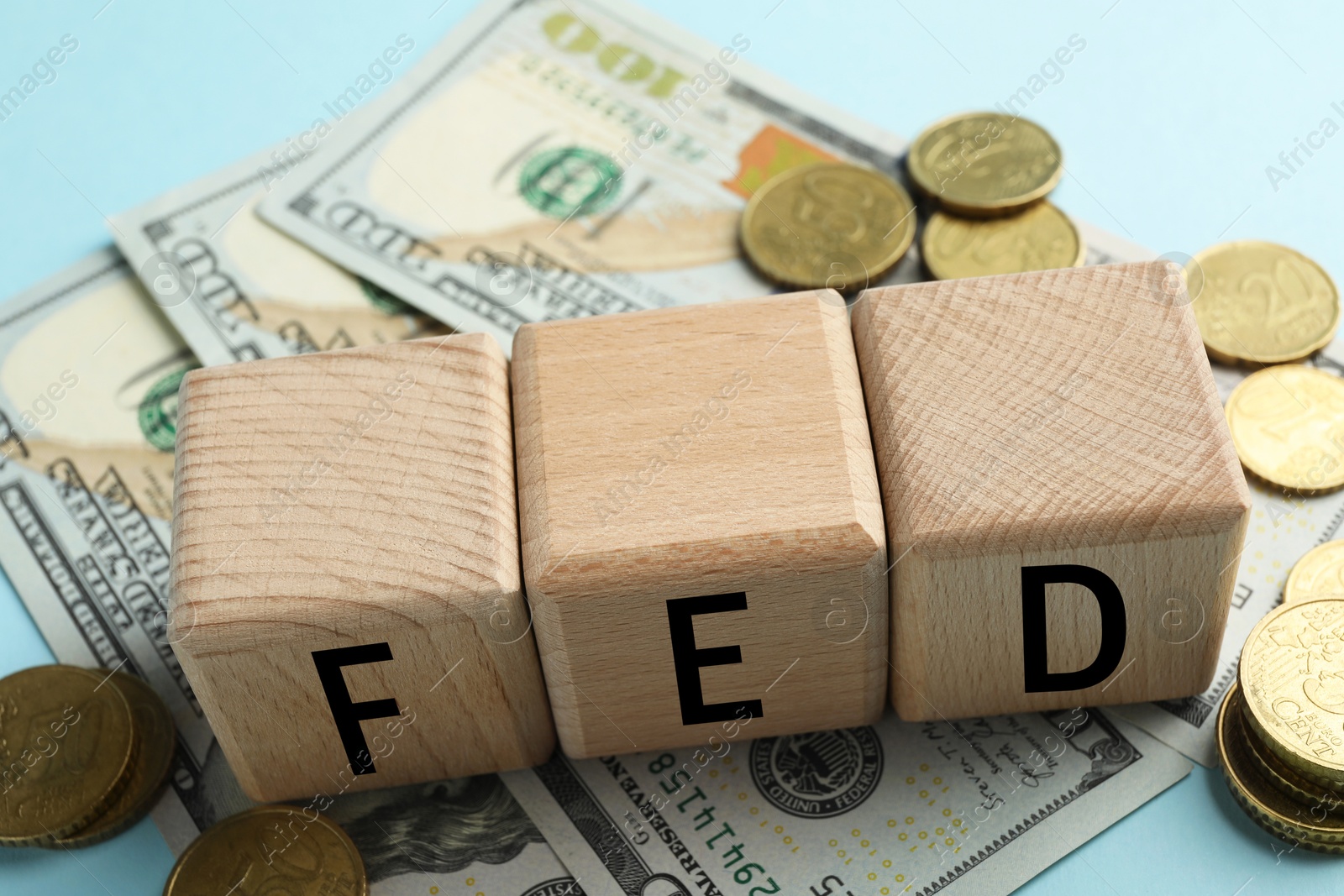 Photo of Wooden cubes with letters Fed (Federal Reserve System), coins and dollar banknotes on light blue background, closeup