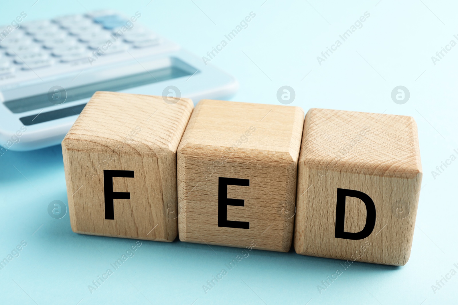 Photo of Wooden cubes with letters Fed (Federal Reserve System) and calculator on light blue background, closeup