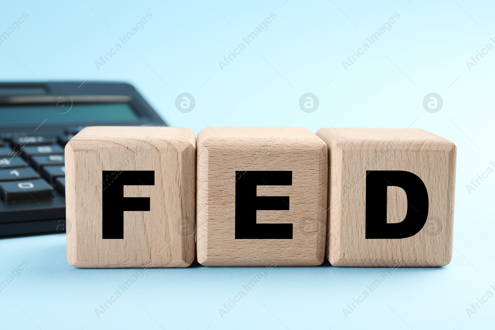 Photo of Wooden cubes with letters Fed (Federal Reserve System) and calculator on light blue background, closeup