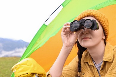 Photo of Young camper with binoculars and tent in mountains, space for text. Active tourism