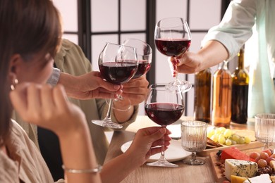 Photo of People clinking glasses of red wine at served table, closeup