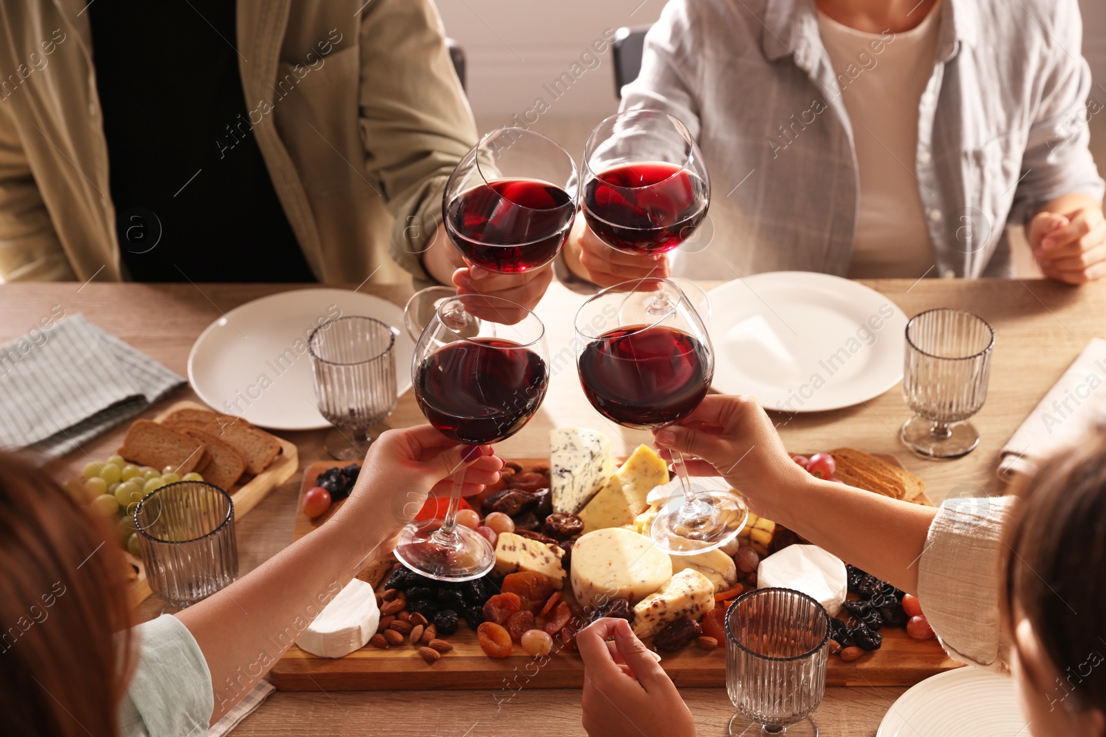 Photo of People clinking glasses of red wine at served table, closeup