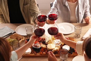 Photo of People clinking glasses of red wine at served table, closeup