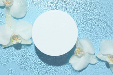 Photo of Beautiful orchid flowers and podium in water on light blue background, flat lay. Presentation for product