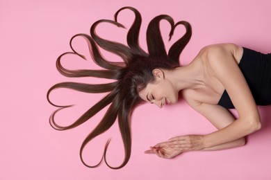 Photo of Beautiful young woman with hair in shape of hearts on pink background, top view