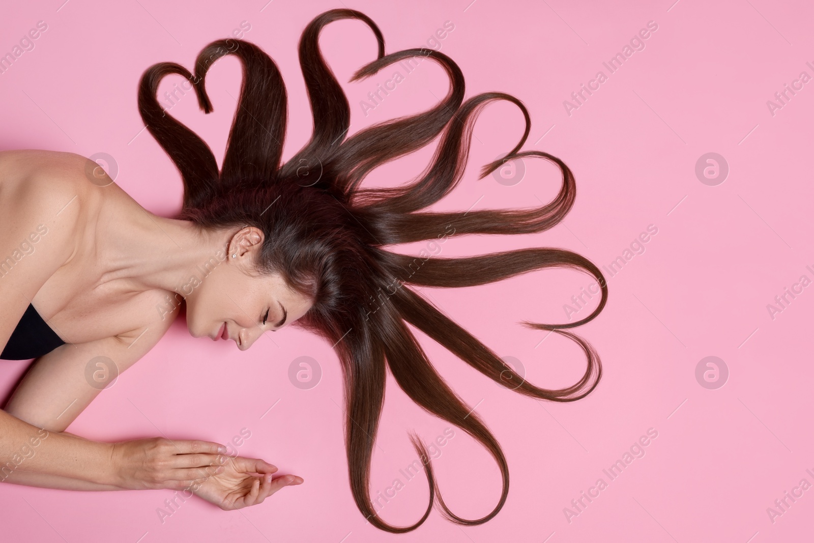 Photo of Beautiful young woman with hair in shape of hearts on pink background, top view