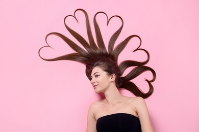 Photo of Beautiful young woman with hair in shape of hearts on pink background, top view