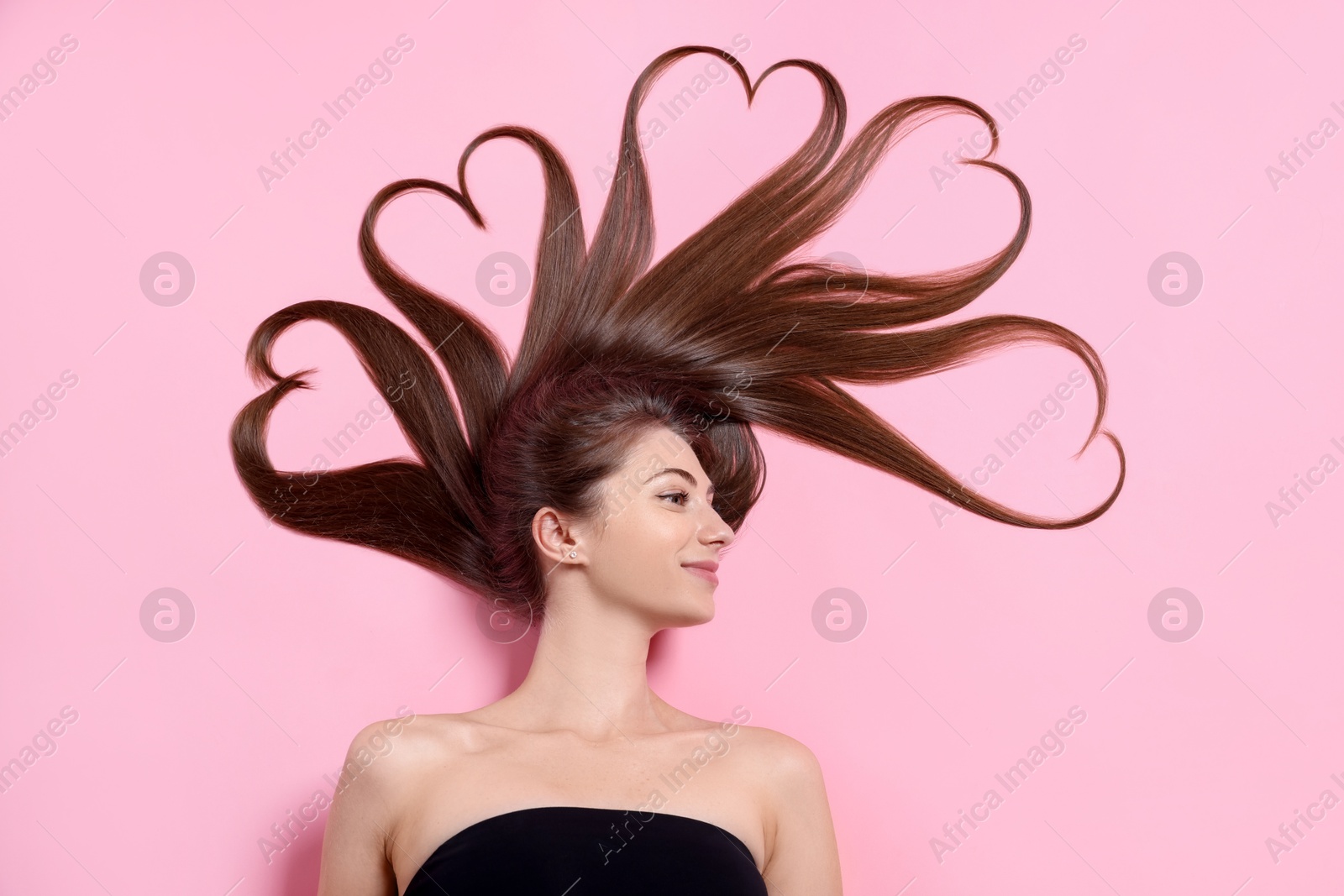 Photo of Beautiful young woman with hair in shape of hearts on pink background, top view