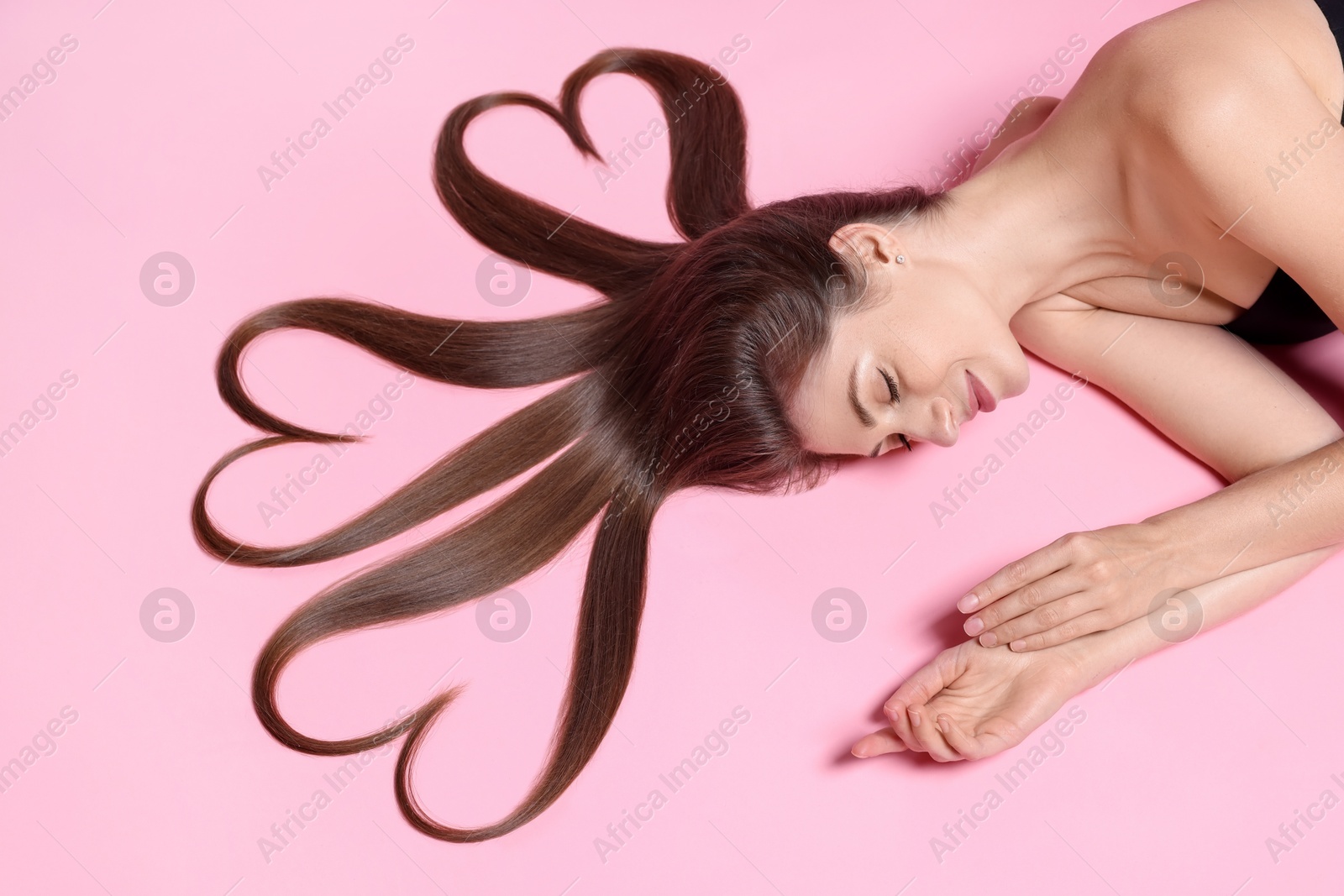 Photo of Beautiful young woman with hair in shape of hearts on pink background