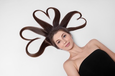 Beautiful young woman with hair in shape of hearts on white background, top view