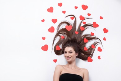 Photo of Beautiful young woman with long hair and red paper hearts on white background, top view