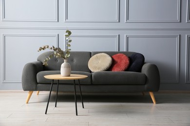 Stylish sofa with cushions and eucalyptus branches in vase on coffee table in room