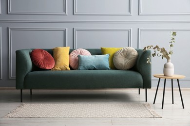 Photo of Stylish sofa with cushions and eucalyptus branches in vase on side table near grey wall