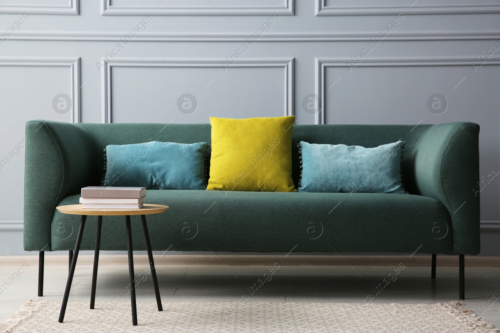 Photo of Stylish sofa with cushions and books on coffee table in room