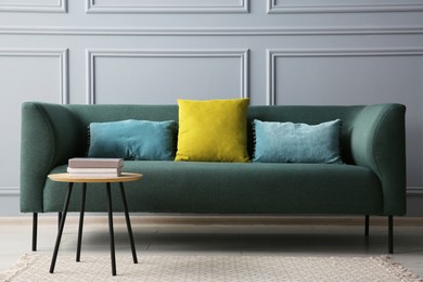 Stylish sofa with cushions and books on coffee table in room