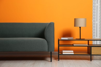 Photo of Stylish sofa and lamp with books on coffee table near orange wall