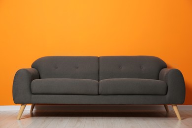 One stylish grey sofa near orange wall