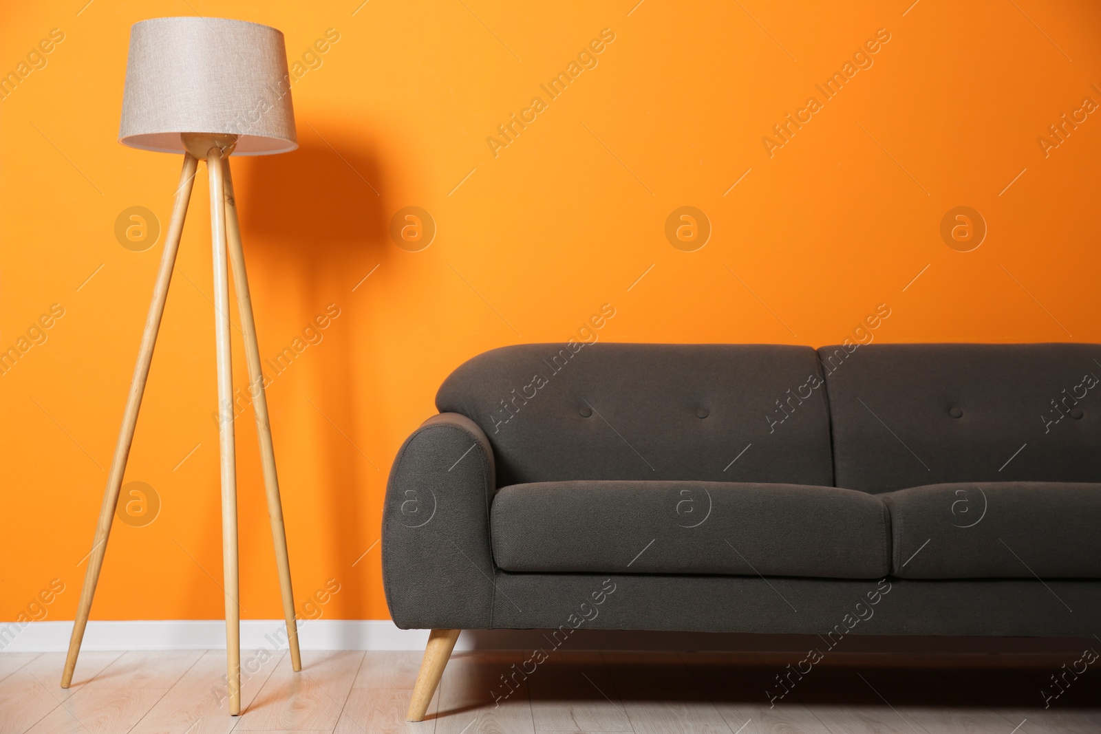 Photo of Stylish sofa and floor lamp near orange wall