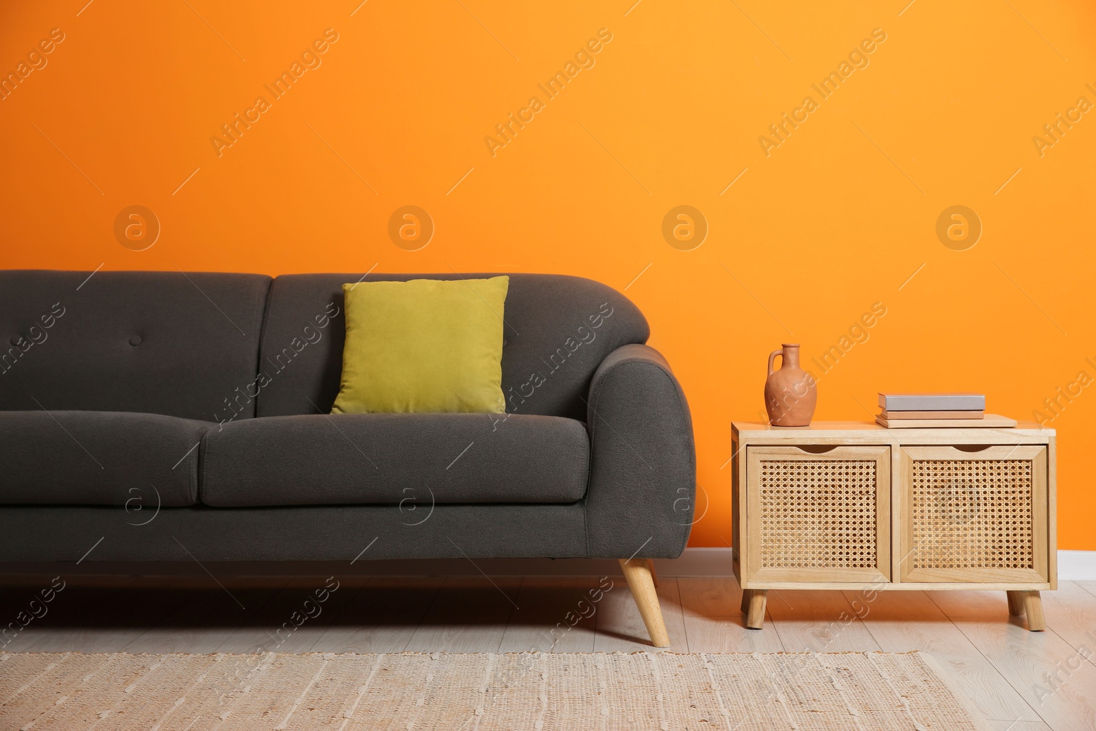 Photo of Stylish sofa with cushion and books on side table near orange wall