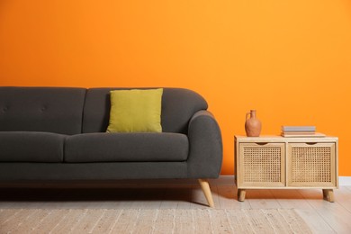 Photo of Stylish sofa with cushion and books on side table near orange wall