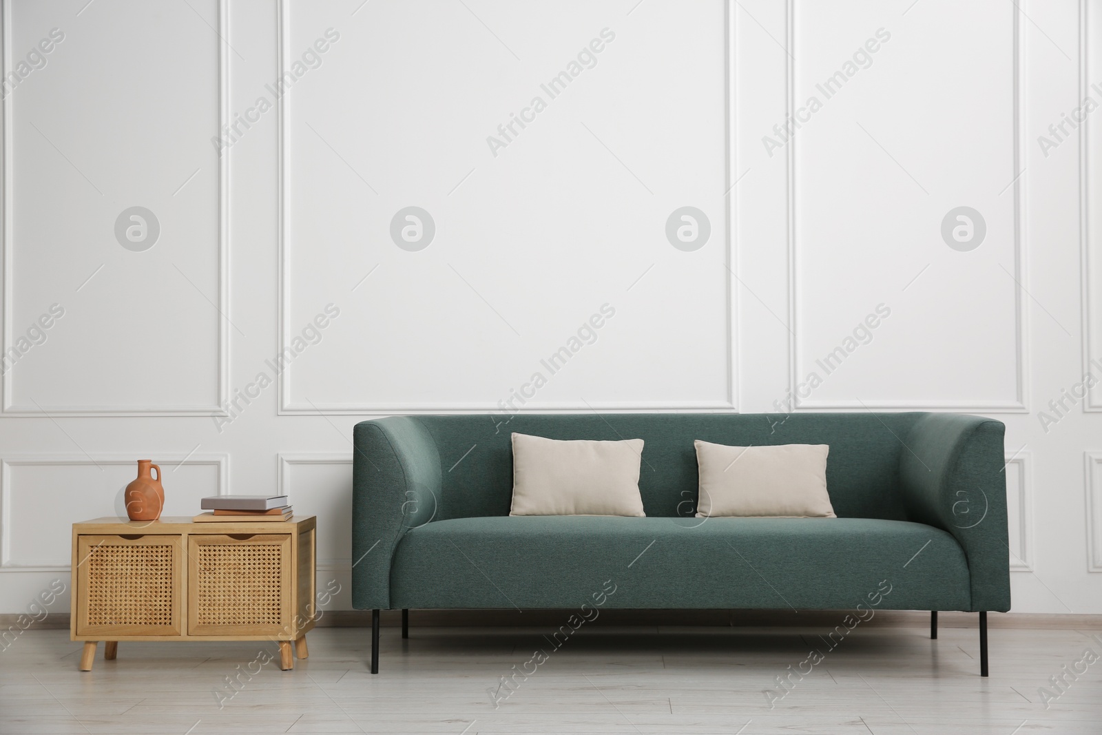 Photo of Stylish sofa with cushions and books on side table near white wall