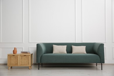 Stylish sofa with cushions and books on side table near white wall