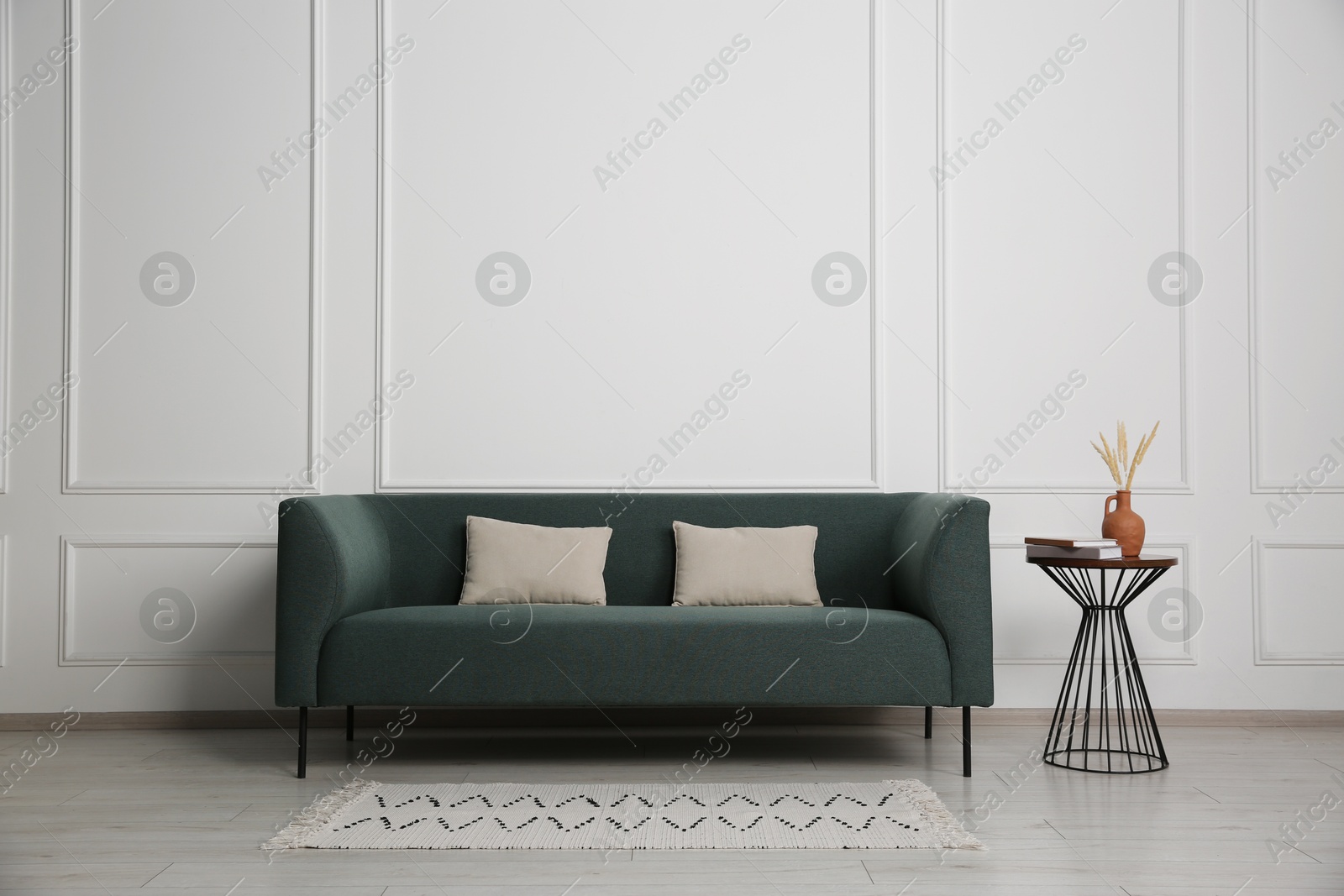 Photo of Stylish sofa, pillows and side table with decor near white wall indoors