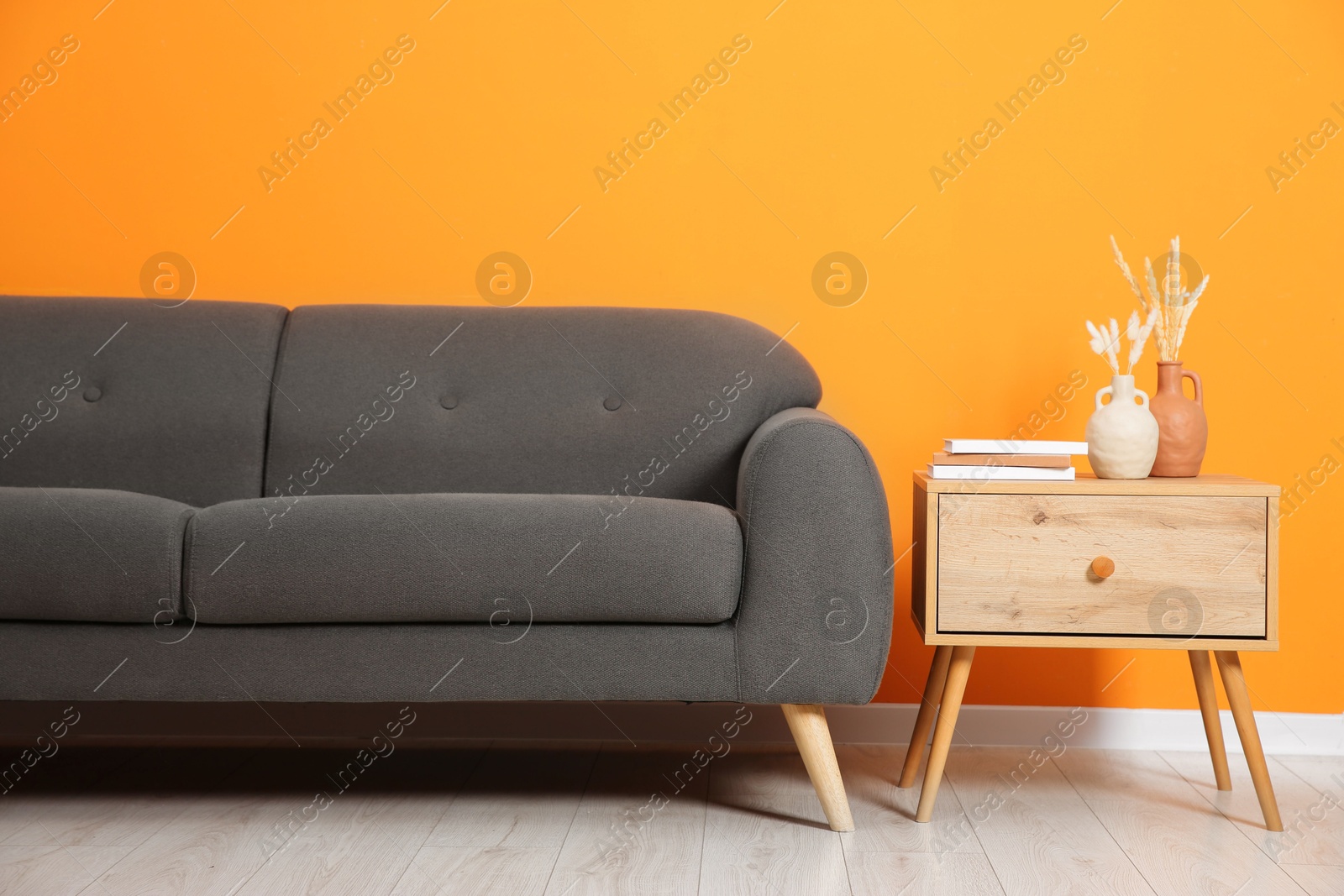 Photo of Stylish sofa and side table with decor near orange wall indoors