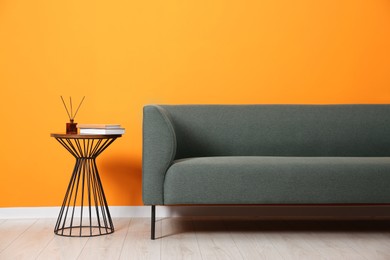 Photo of Stylish sofa and side table with decor near orange wall indoors