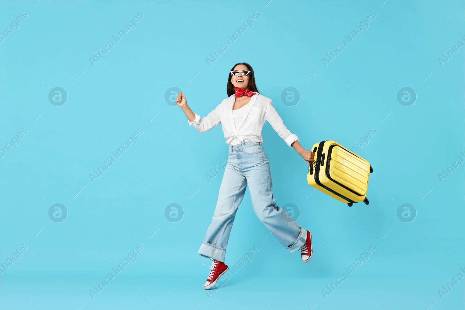 Photo of Happy young woman in sunglasses with suitcase on light blue background