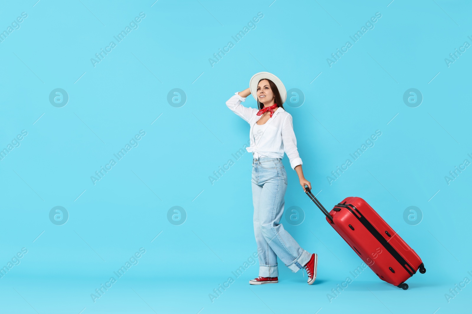 Photo of Happy young woman with suitcase on light blue background, space for text