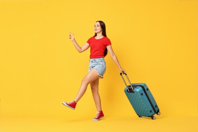 Photo of Happy young woman with suitcase walking on orange background