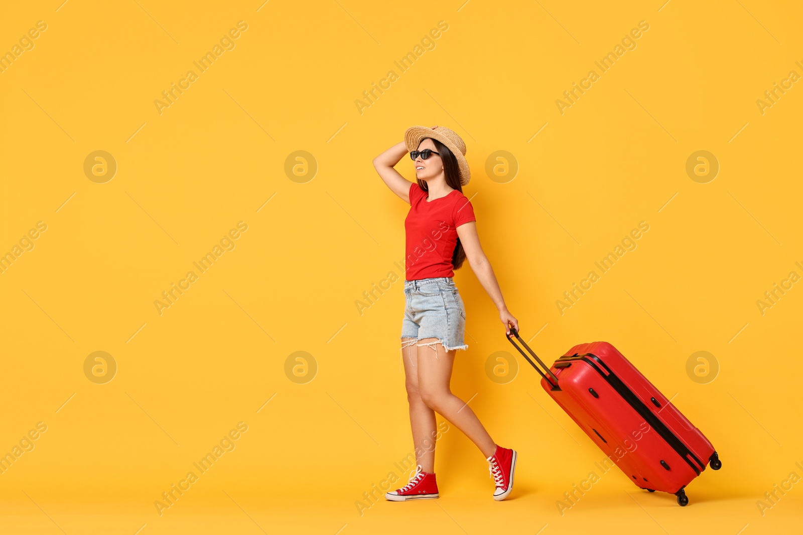 Photo of Happy young woman in sunglasses with suitcase on orange background