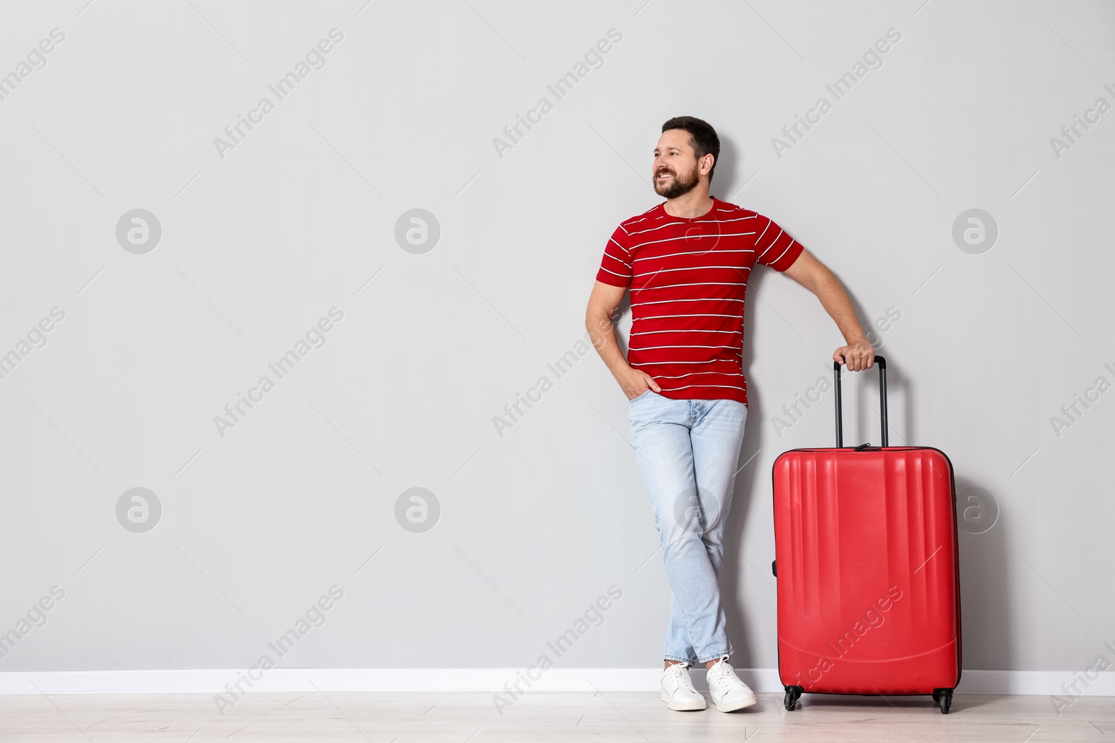 Photo of Happy man with suitcase near light gray wall indoors, space for text