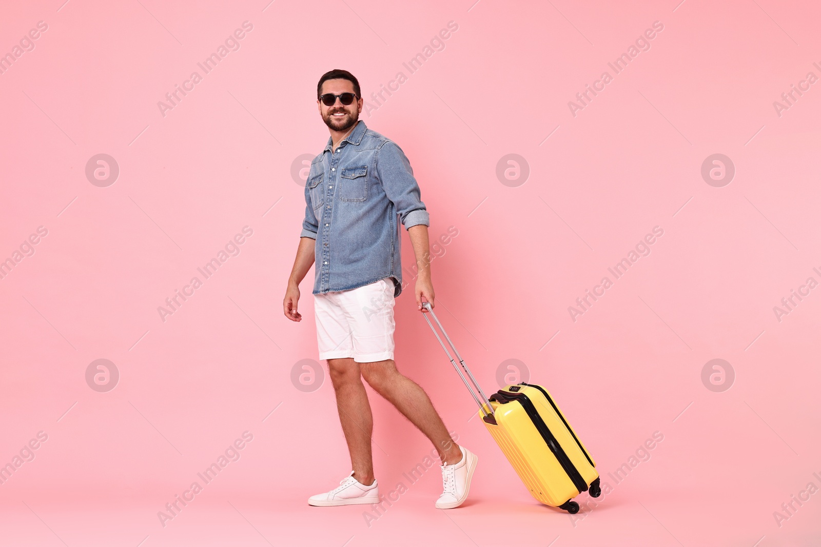 Photo of Happy man in sunglasses with suitcase on pink background