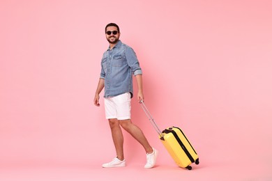 Happy man in sunglasses with suitcase on pink background