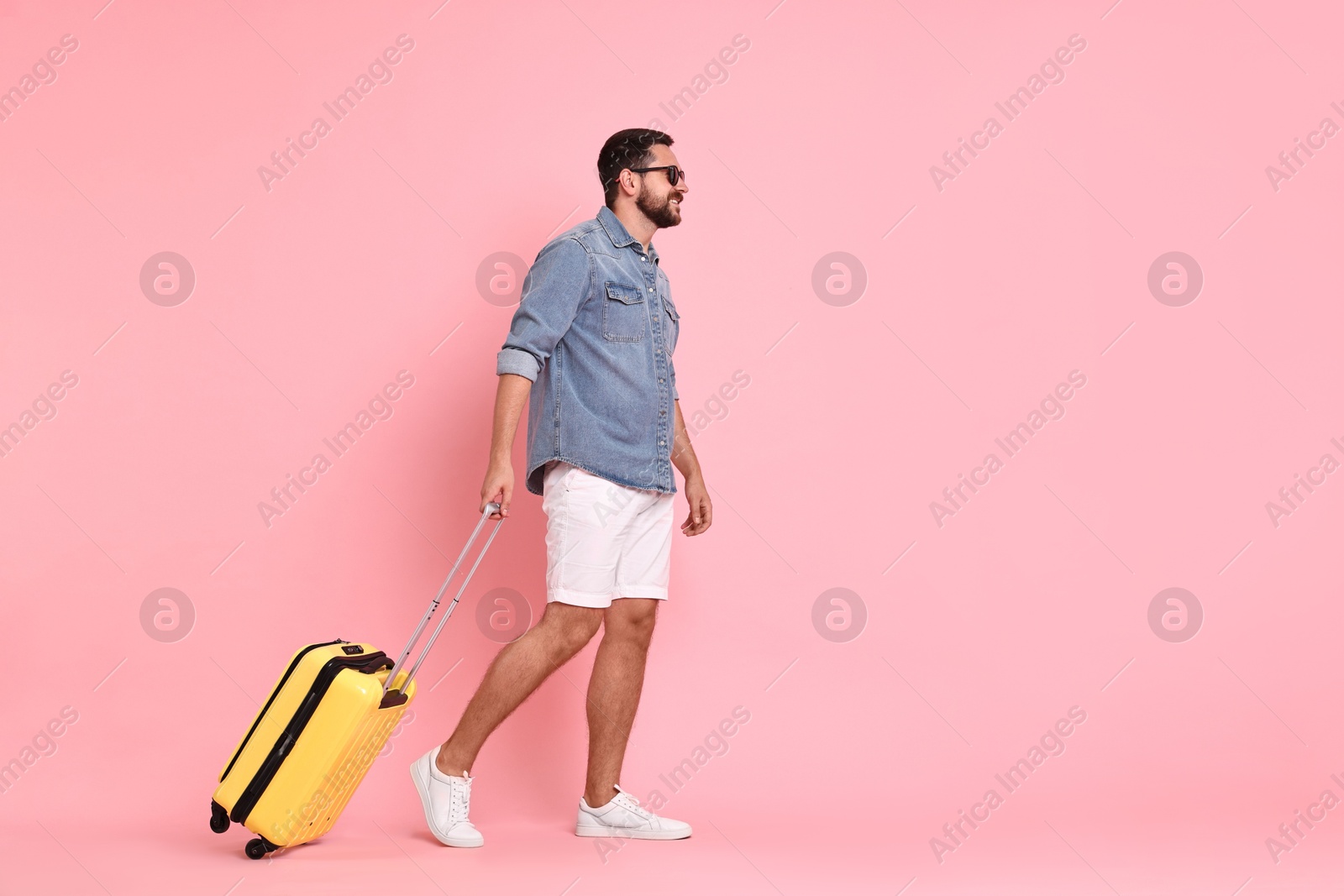 Photo of Happy man in sunglasses with suitcase on pink background