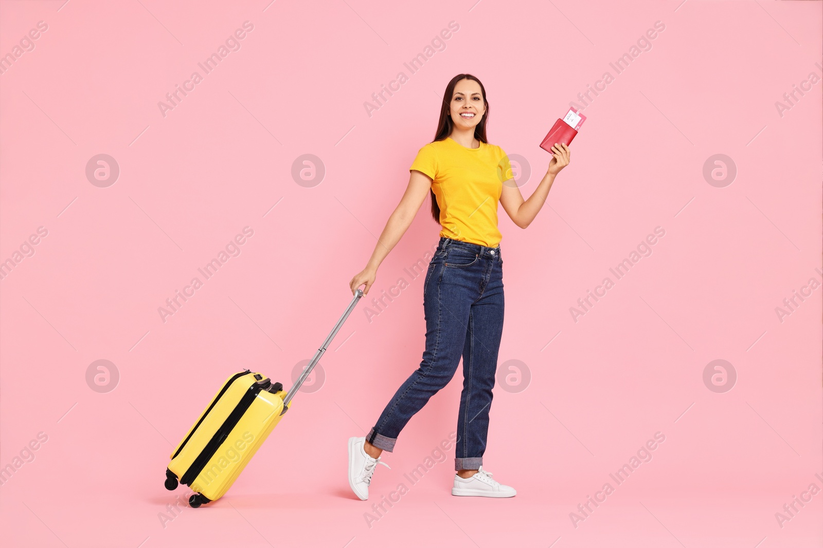 Photo of Happy young woman with suitcase, passport and ticket walking on pink background