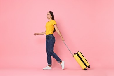 Happy young woman with suitcase walking on pink background