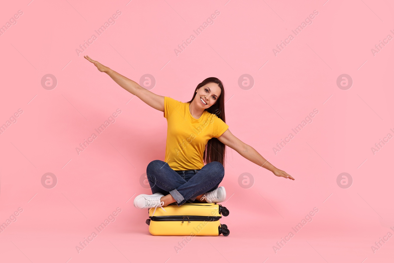 Photo of Happy young woman sitting on suitcase against pink background