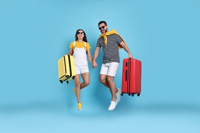 Photo of Happy couple in sunglasses with suitcases jumping on light blue background