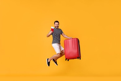 Happy man with suitcase jumping on orange background